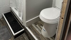 A small bathroom with a shower, toilet, and a metal rack on the wall. - Sub Level Effiency (Geneva)
