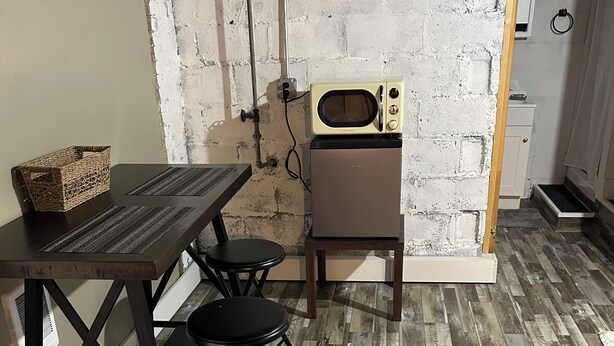 A kitchen with a wooden table, two chairs, a microwave, and a brick wall. - Sub Level Effiency (Geneva)