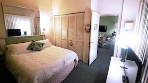 A bedroom with a bed, a wardrobe, a mirror, a desk, and a television.