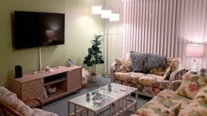 A living room with a flat-screen TV, a sofa, a coffee table, and a potted plant.