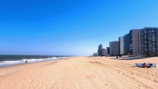 A beach with a clear sky, sandy shore, and high-rise buildings in the background.