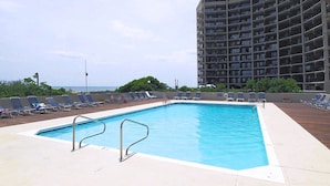 A rectangular swimming pool with two metal ladders, surrounded by lounge chairs and a high-rise building in the background.