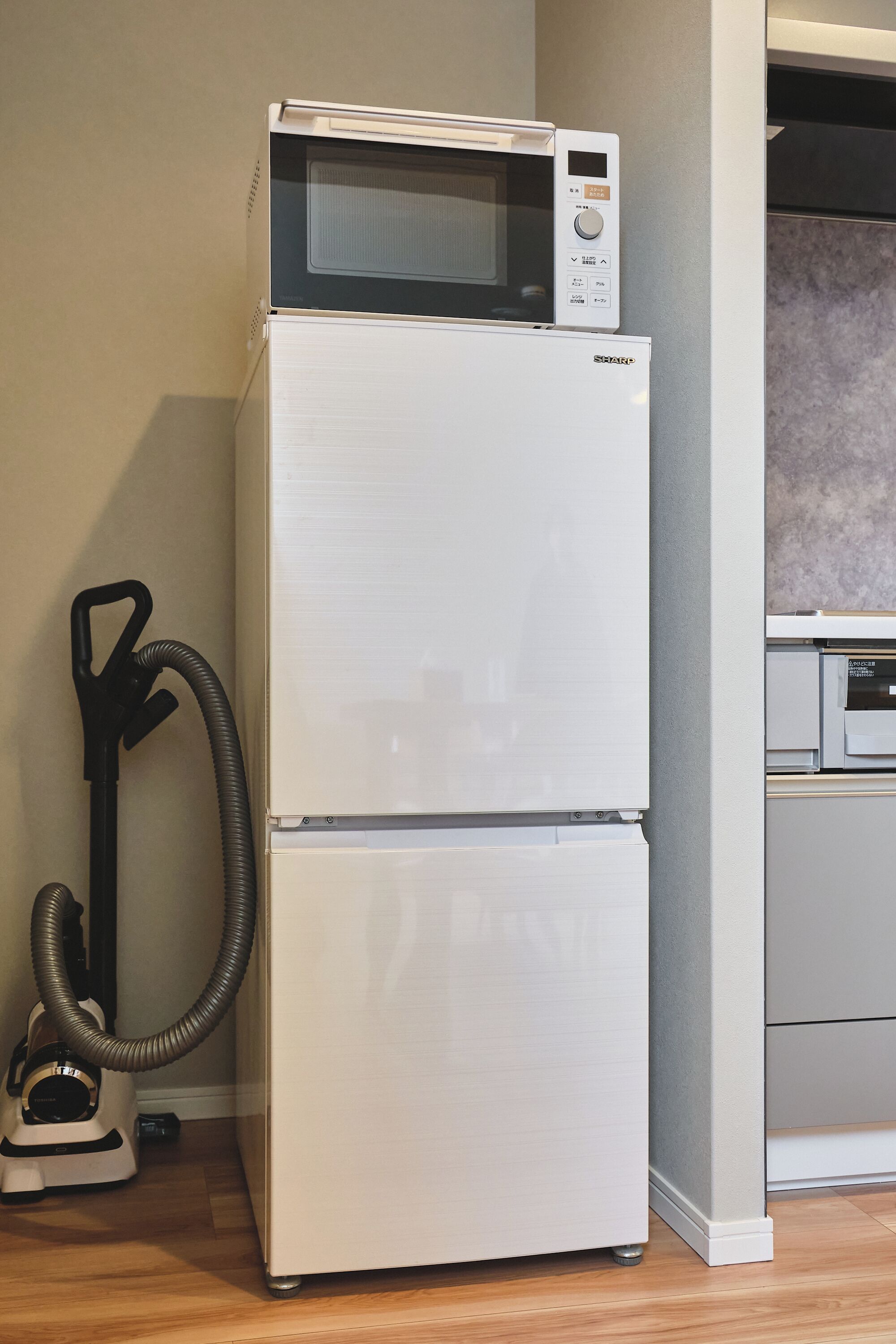 A white refrigerator with a microwave on top, a vacuum cleaner, and a dishwasher in a kitchen.