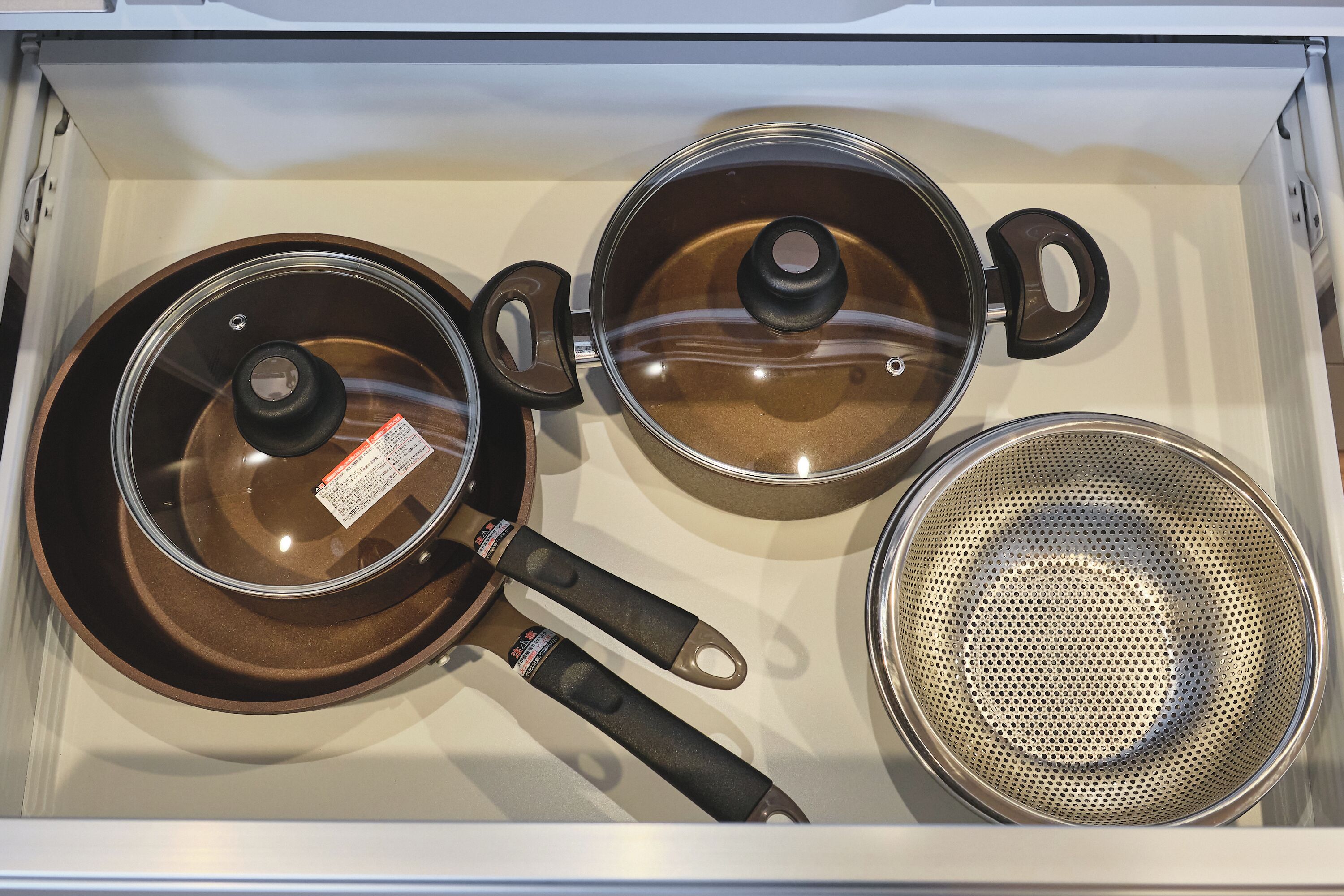 A kitchen drawer with two pots and a colander.