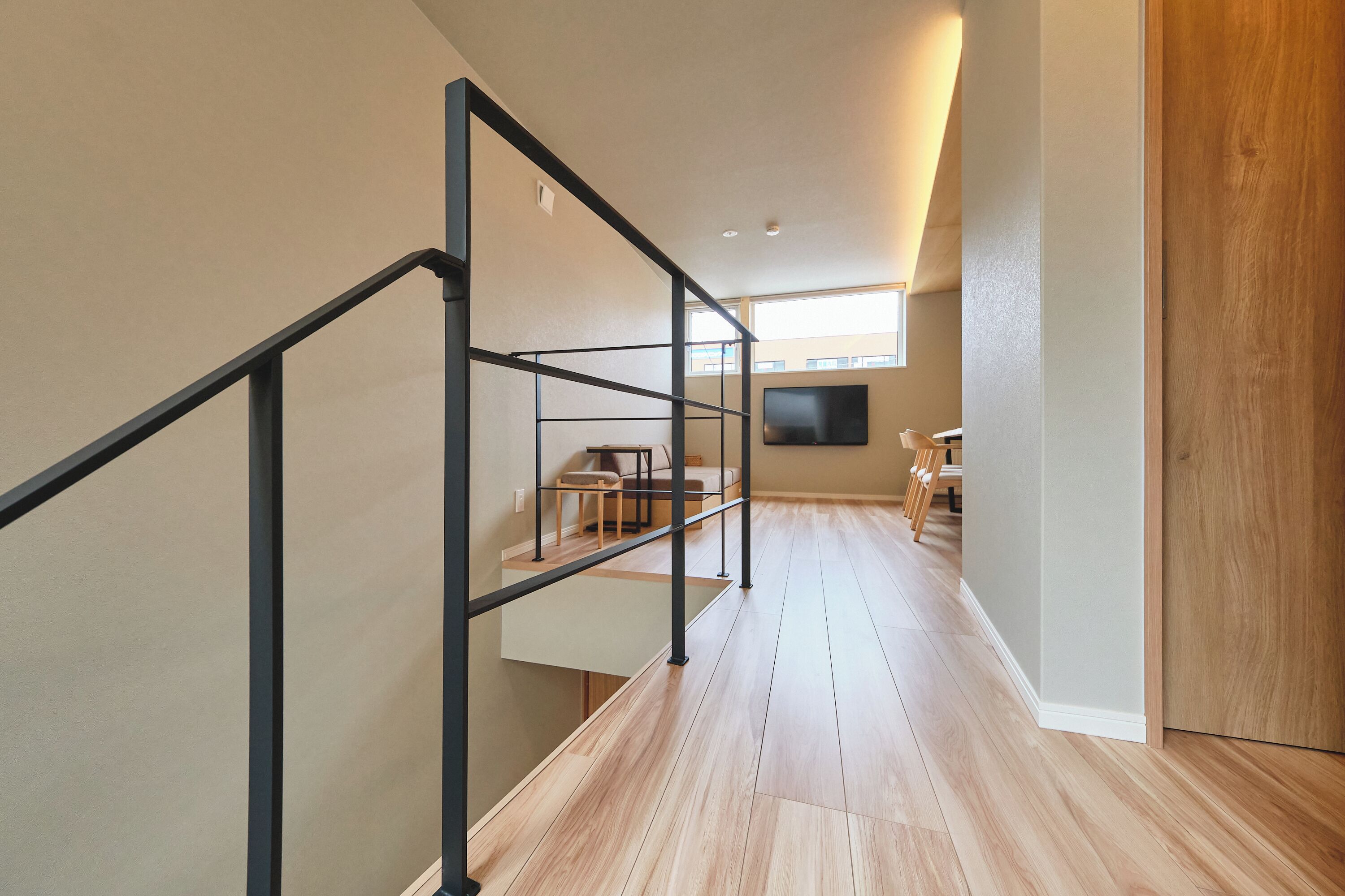 A modern interior with a staircase, wooden flooring, and a dining area with chairs and a table.