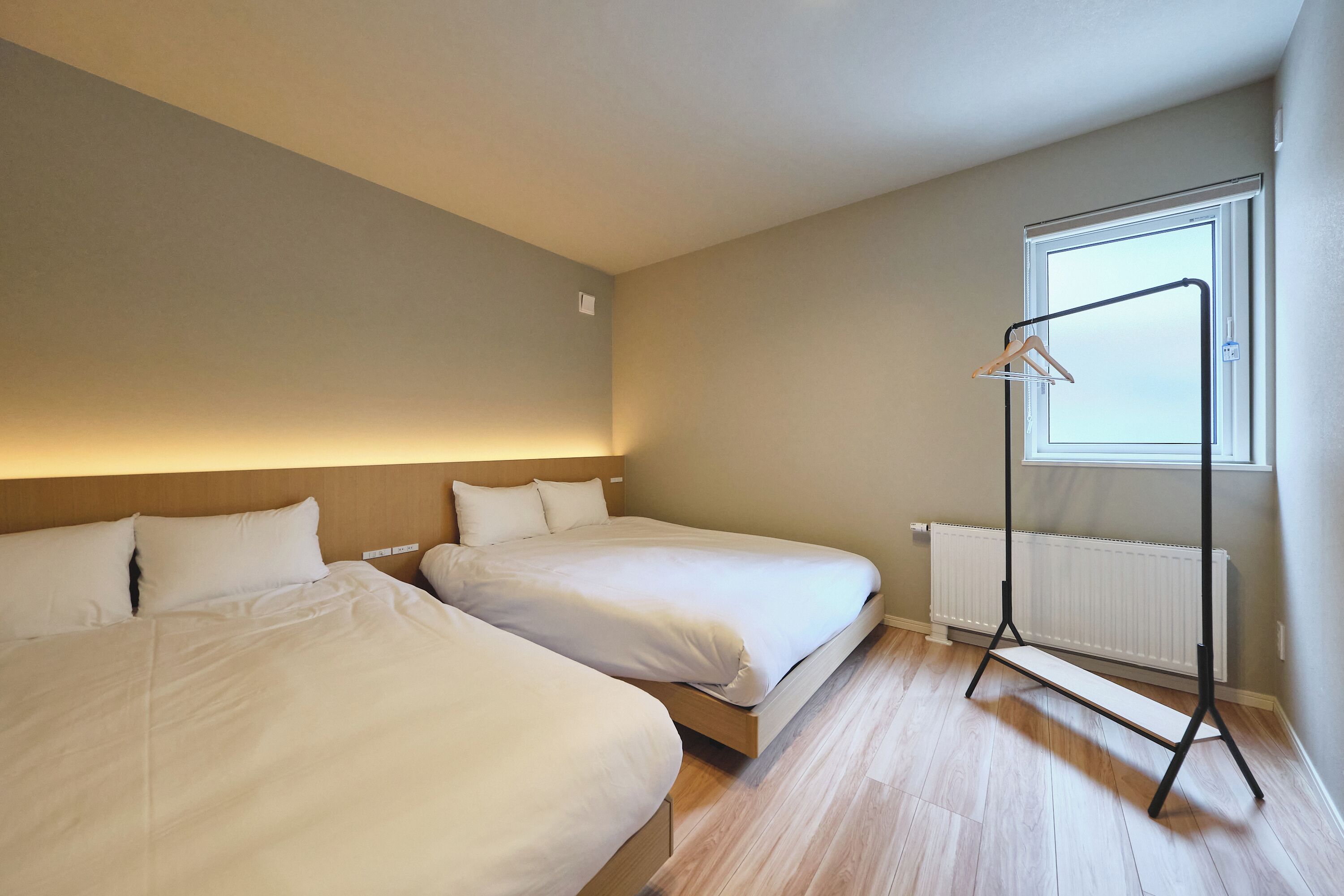 A bedroom with two beds, a radiator, a window, and a hanging light fixture.