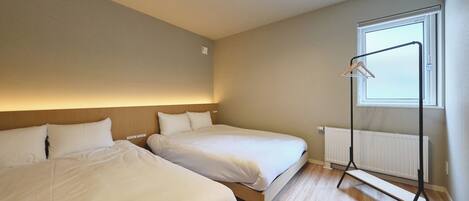 A bedroom with two beds, a radiator, a window, and a hanging light fixture.