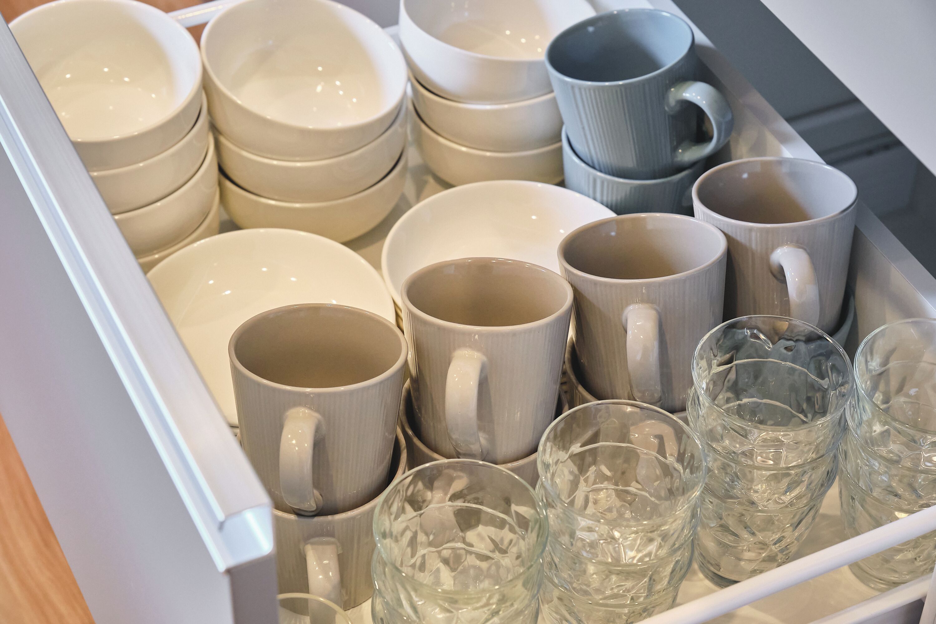 A drawer containing various white and gray ceramic mugs and bowls.