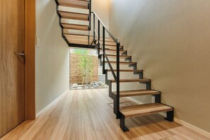 A modern staircase with wooden steps and metal railings, leading to a room with a wooden floor and a view of a garden. - SAUNA STYLE SAPPORO (Sapporo)
