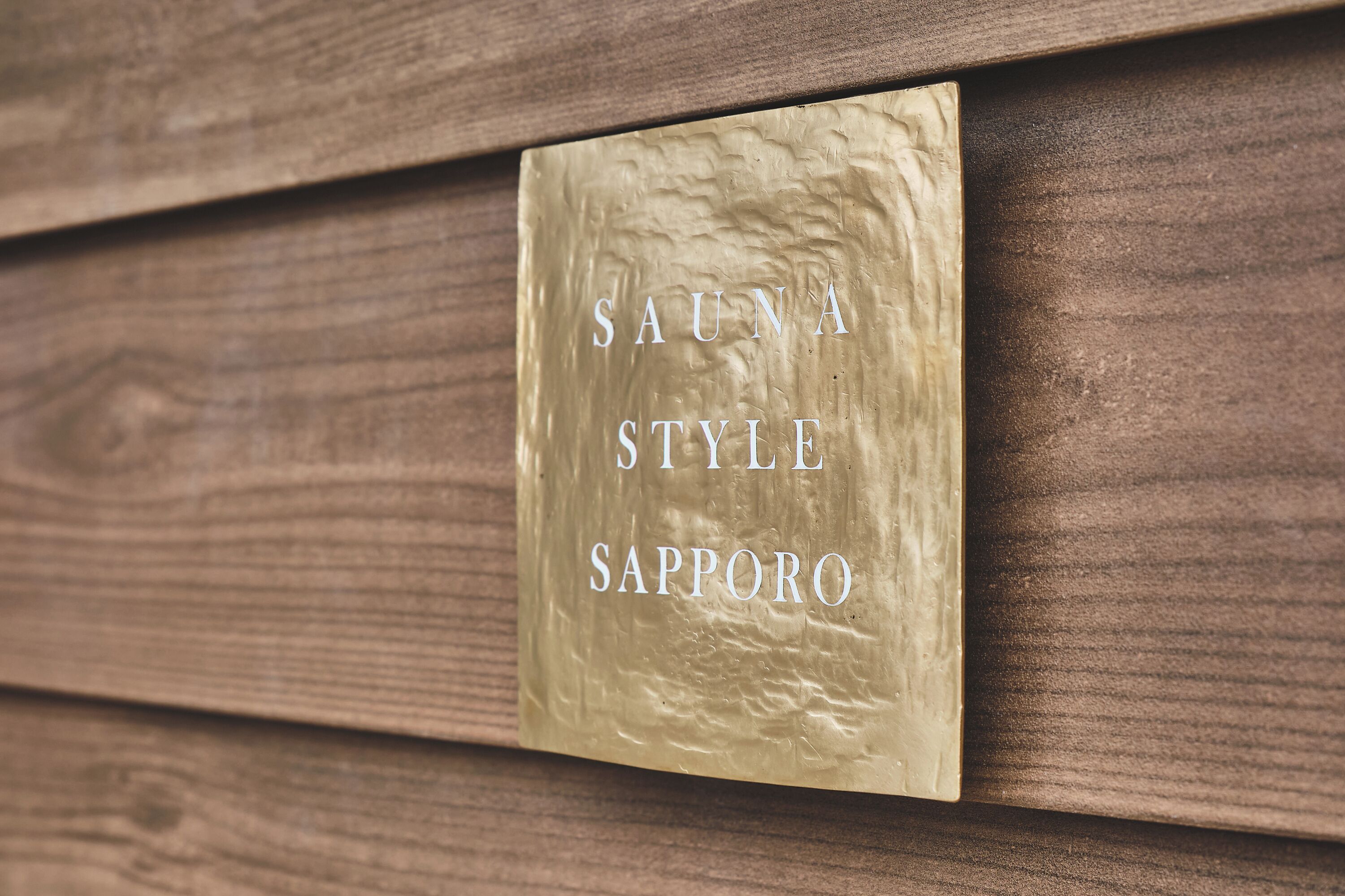 Eine goldene Plakette mit dem Schriftzug "SAUNA STYLE SAPPORO" auf einer Holzfläche.