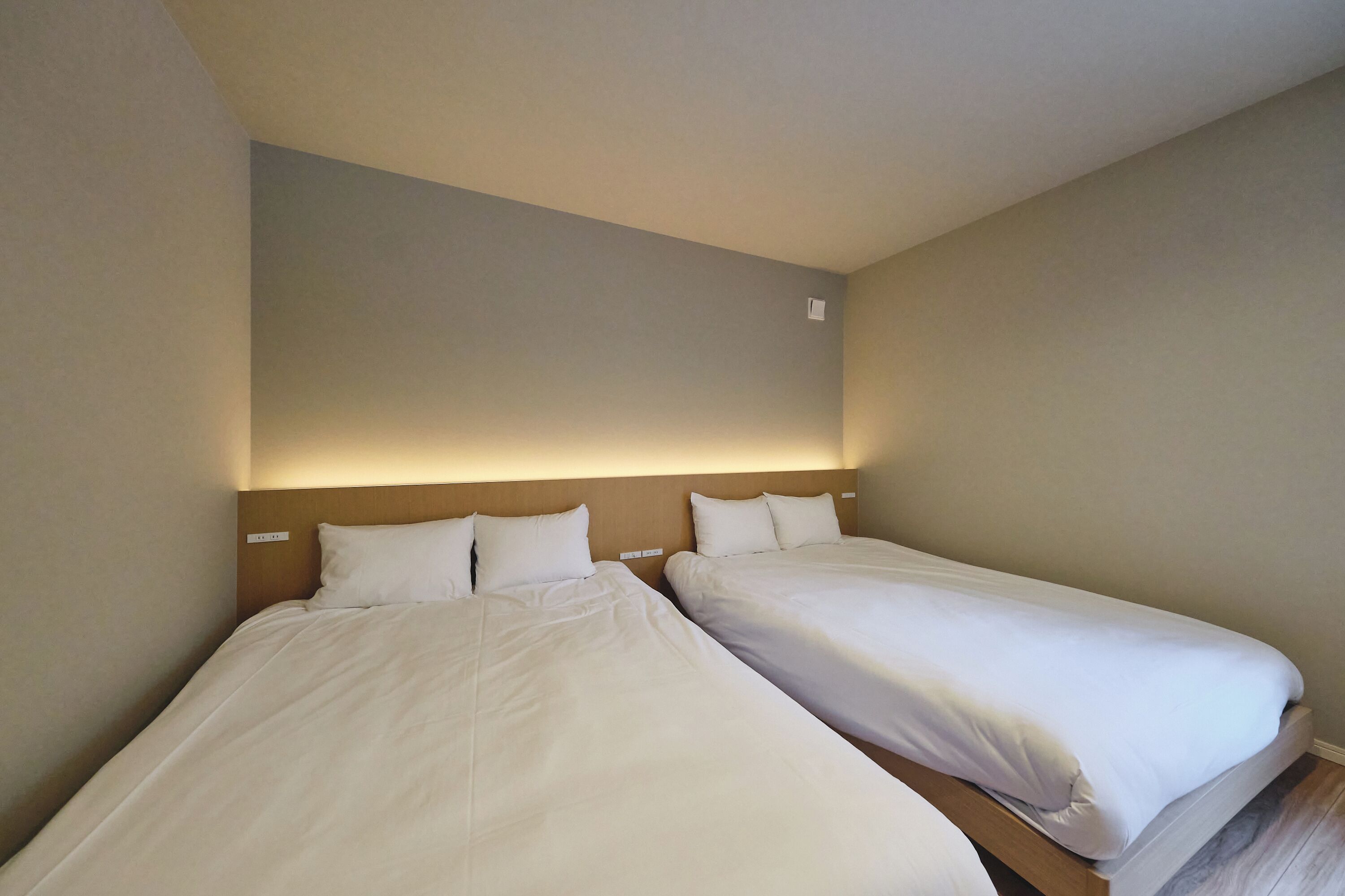 A hotel room with two single beds, a wooden headboard, and a neutral color scheme.