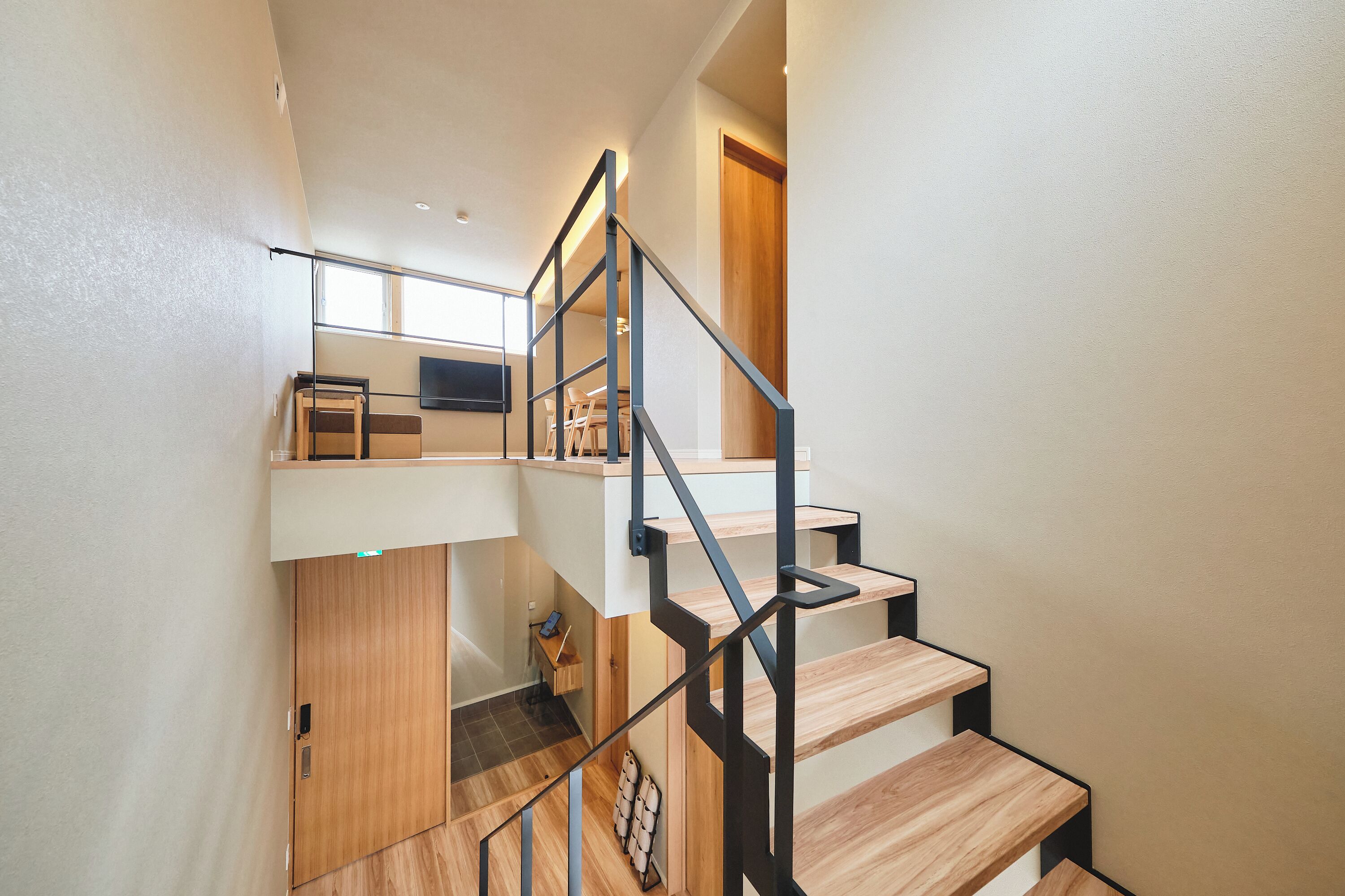 A modern staircase with wooden steps and metal railings, leading to a lofted area with a desk and chair.