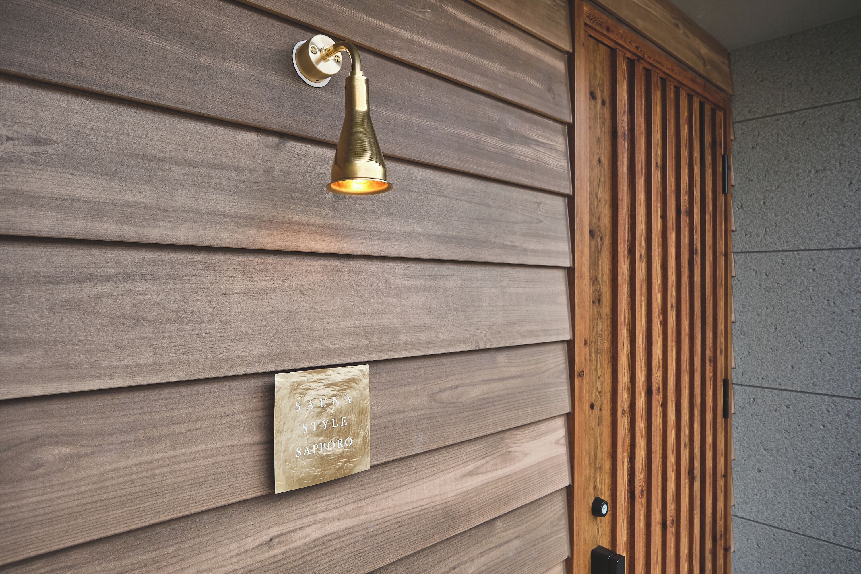 A wall with horizontal wooden panels and a brass wall-mounted light fixture.