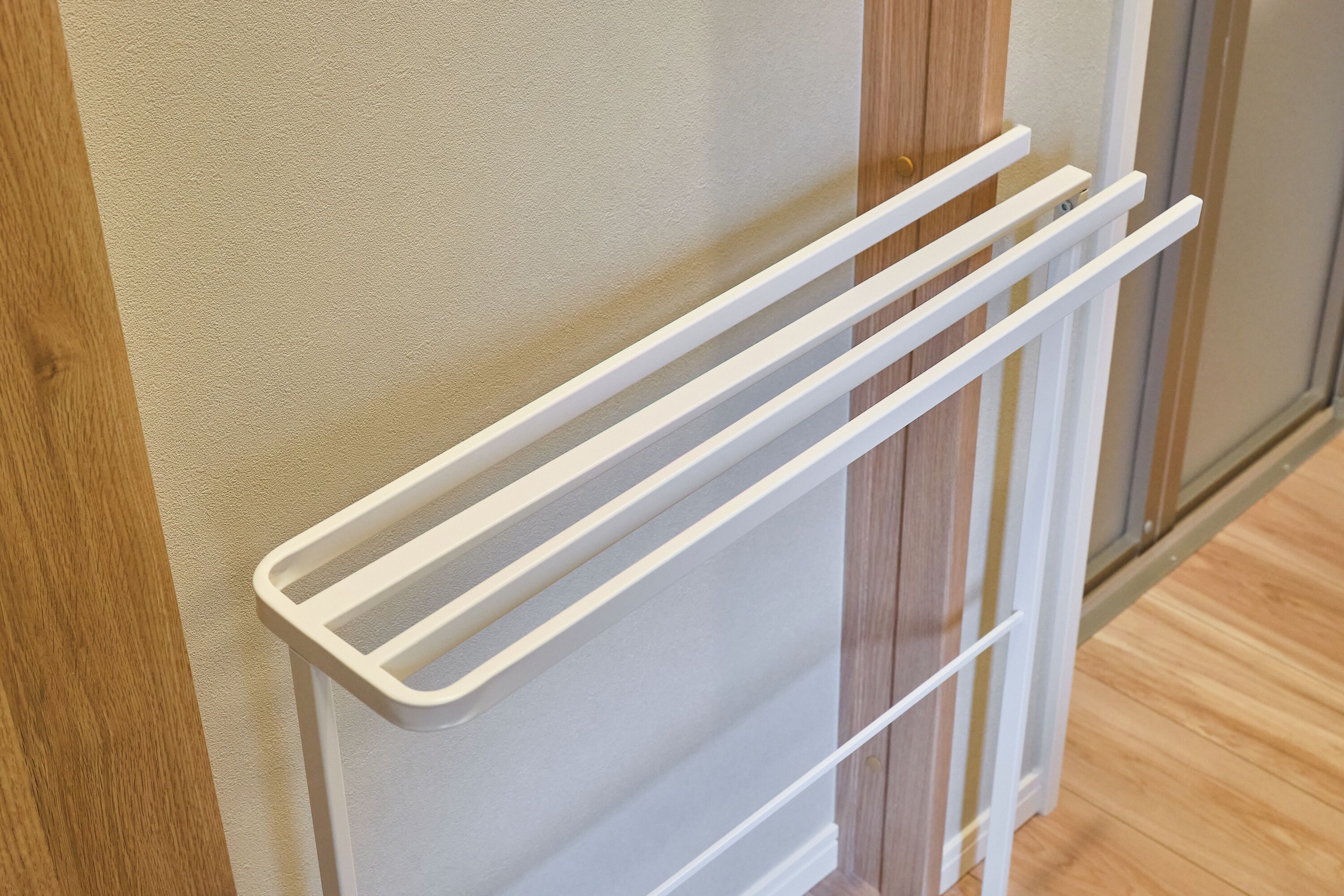 A white towel rack mounted on a wall with a wooden panel.