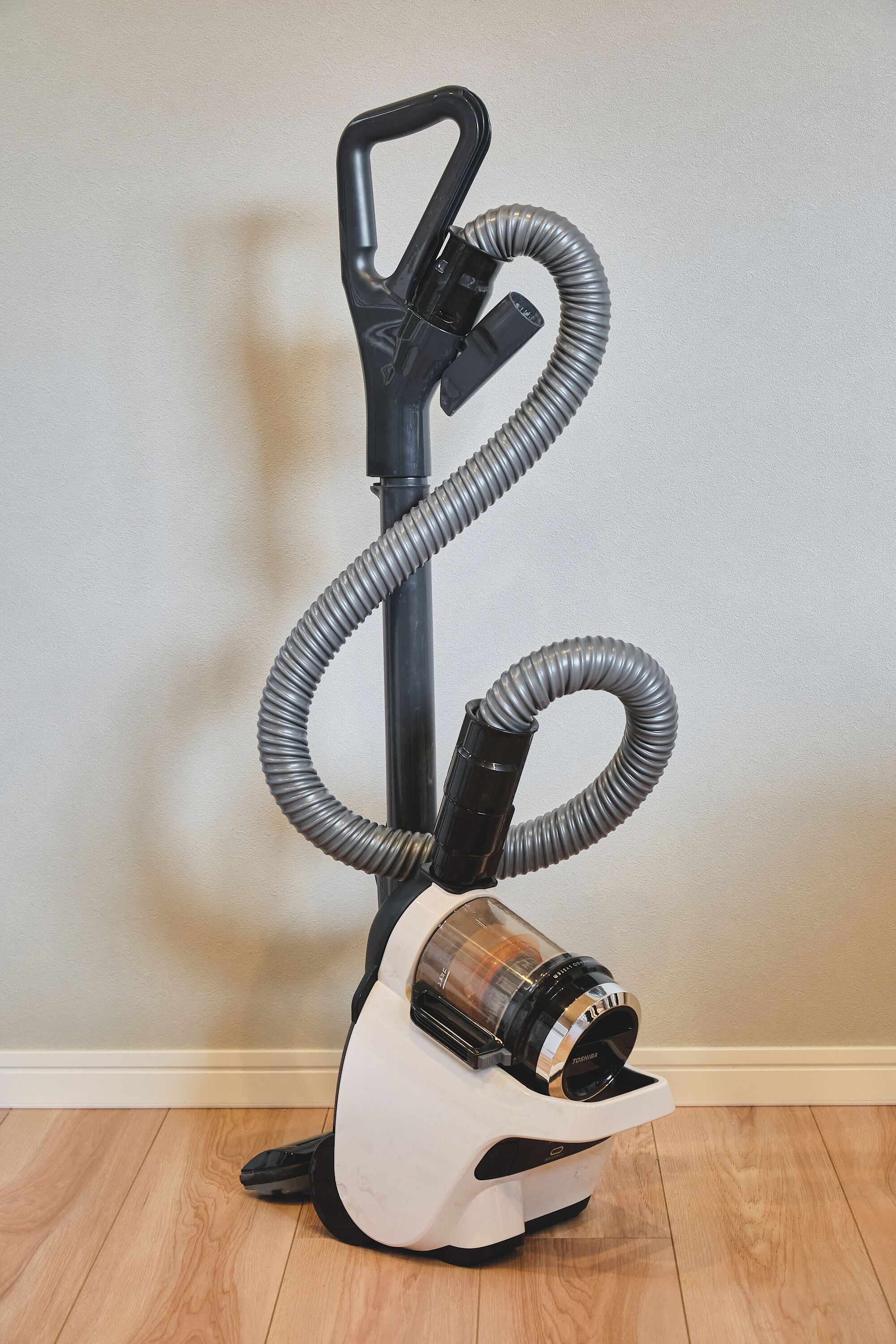 Un aspirateur vertical doté d’un tuyau flexible et d’un récipient à poussière transparent.