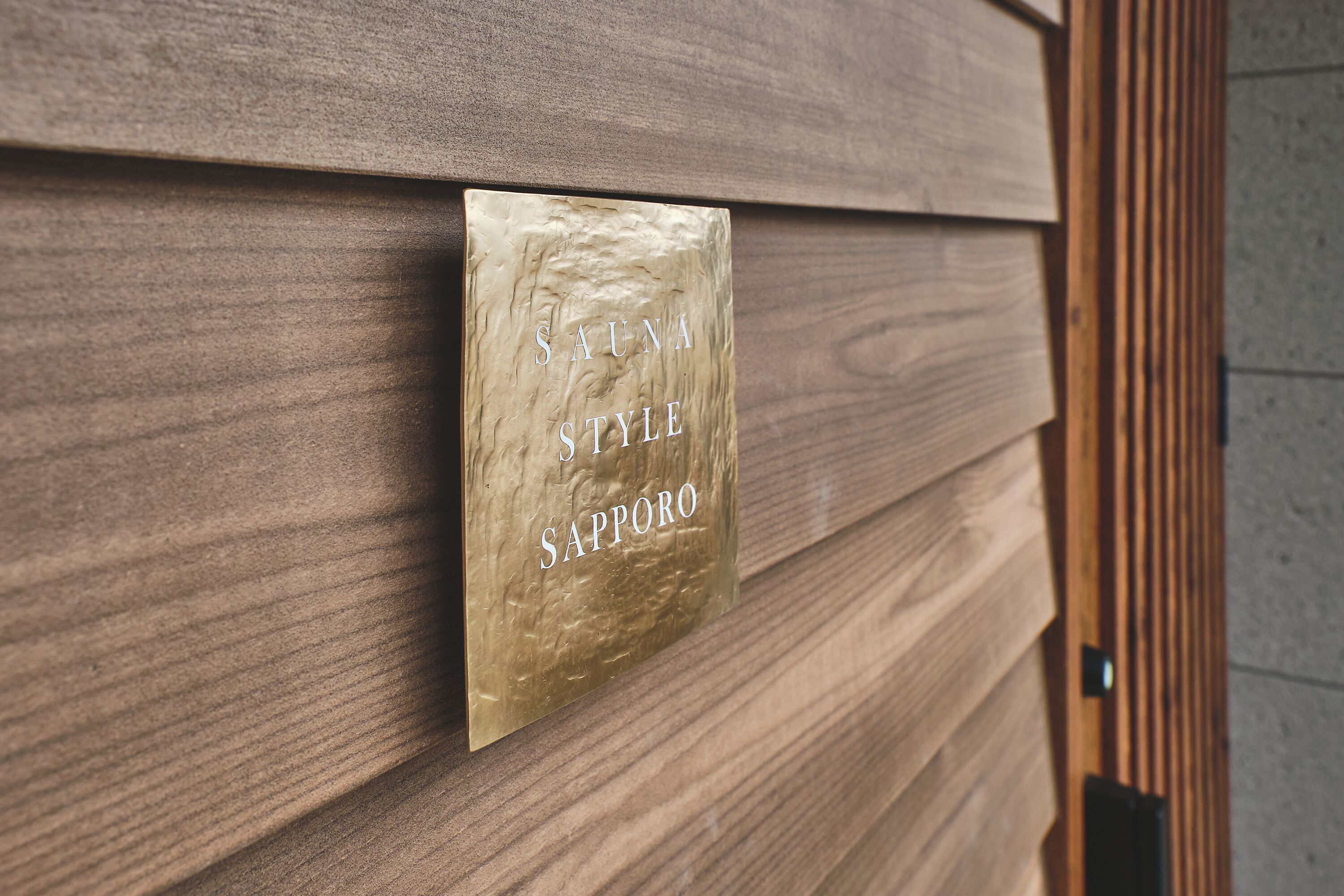 A sign with the text "SAUNA STYLE SAPPORO" on a wooden wall.
