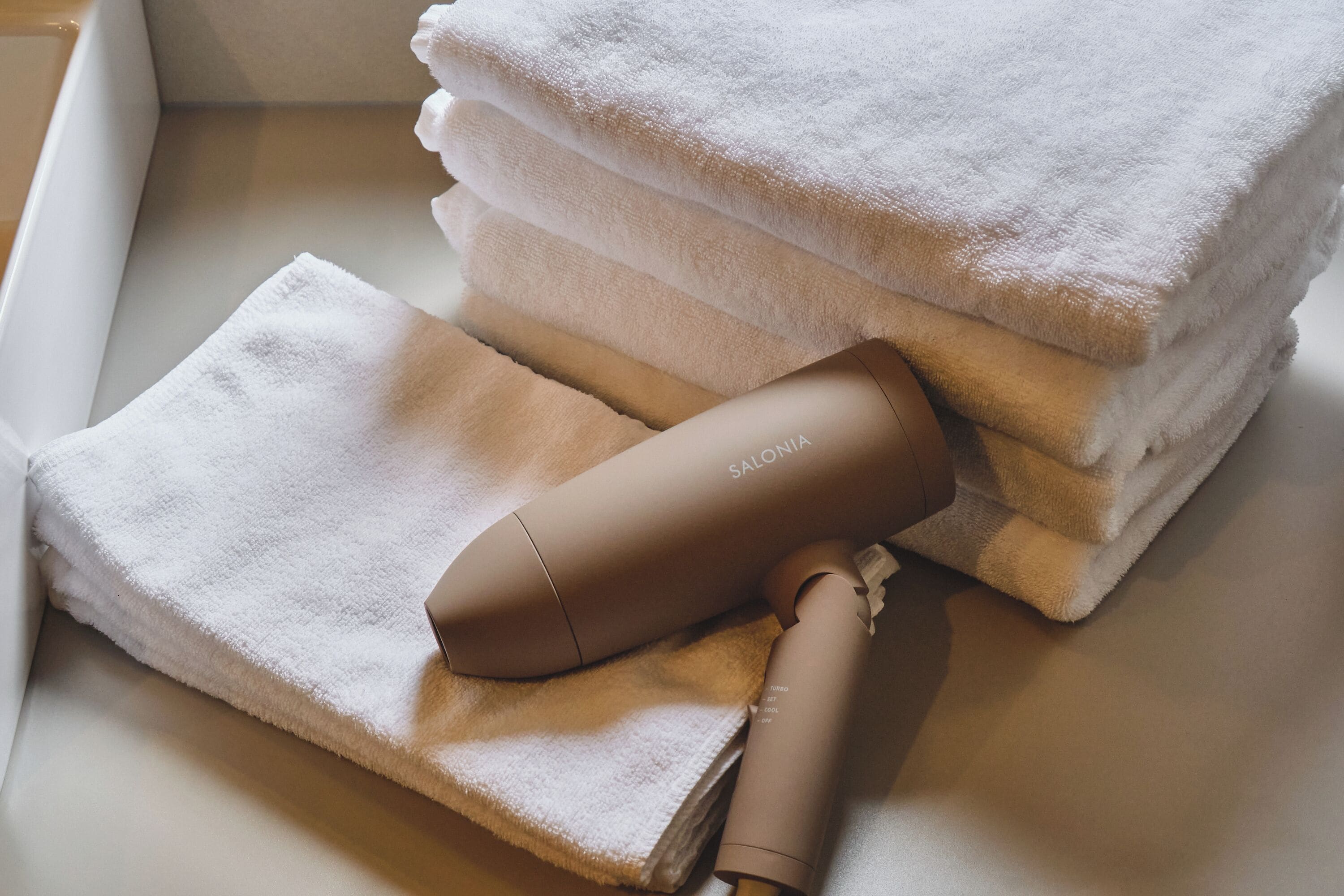 A stack of neatly folded towels and a hairdryer on a white surface.