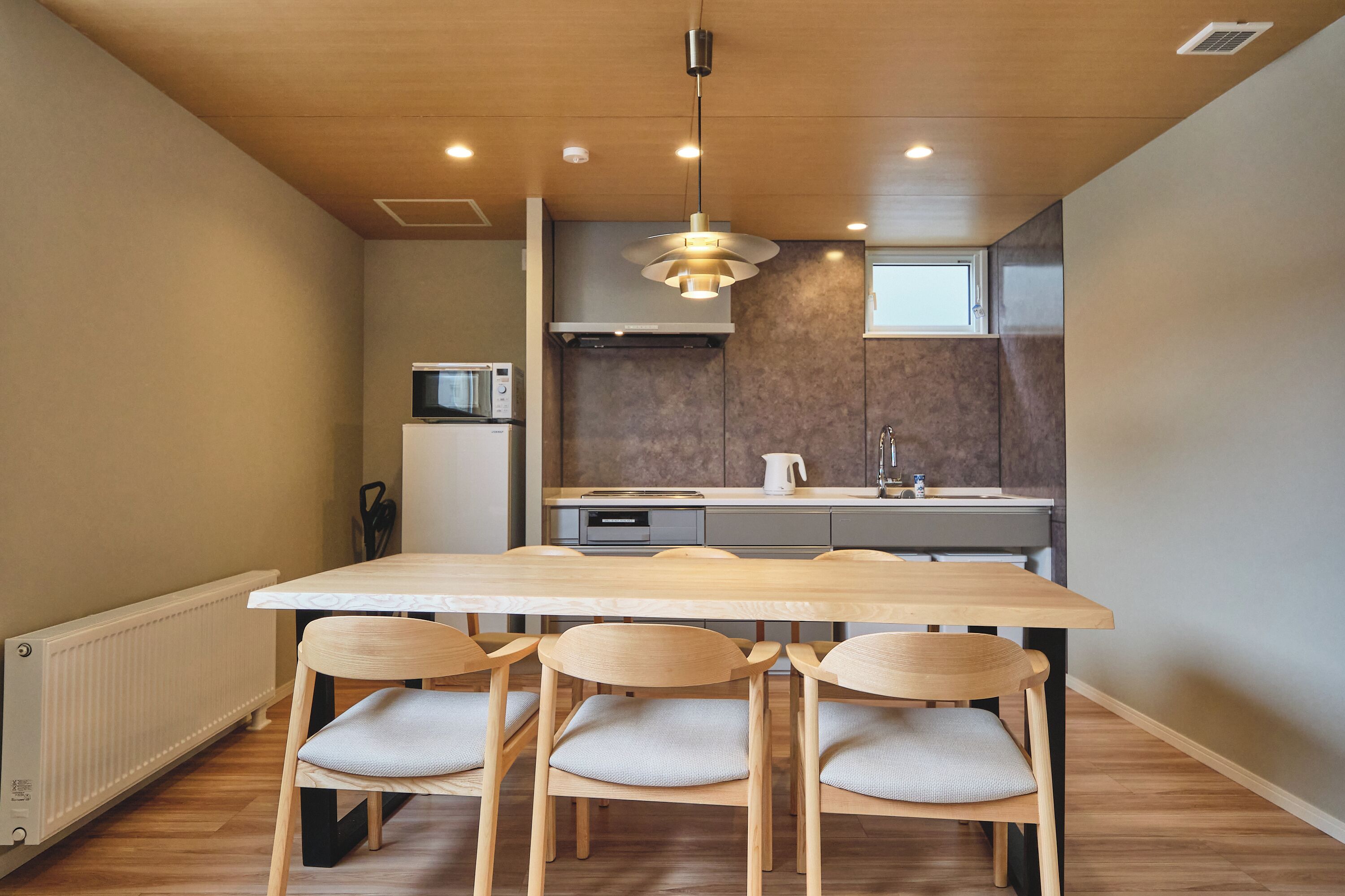 A modern kitchen with a wooden table and chairs, a built-in oven, and a microwave.
