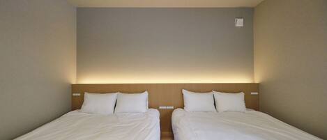 A hotel room with two single beds, a wooden headboard, and a small wall-mounted light fixture.