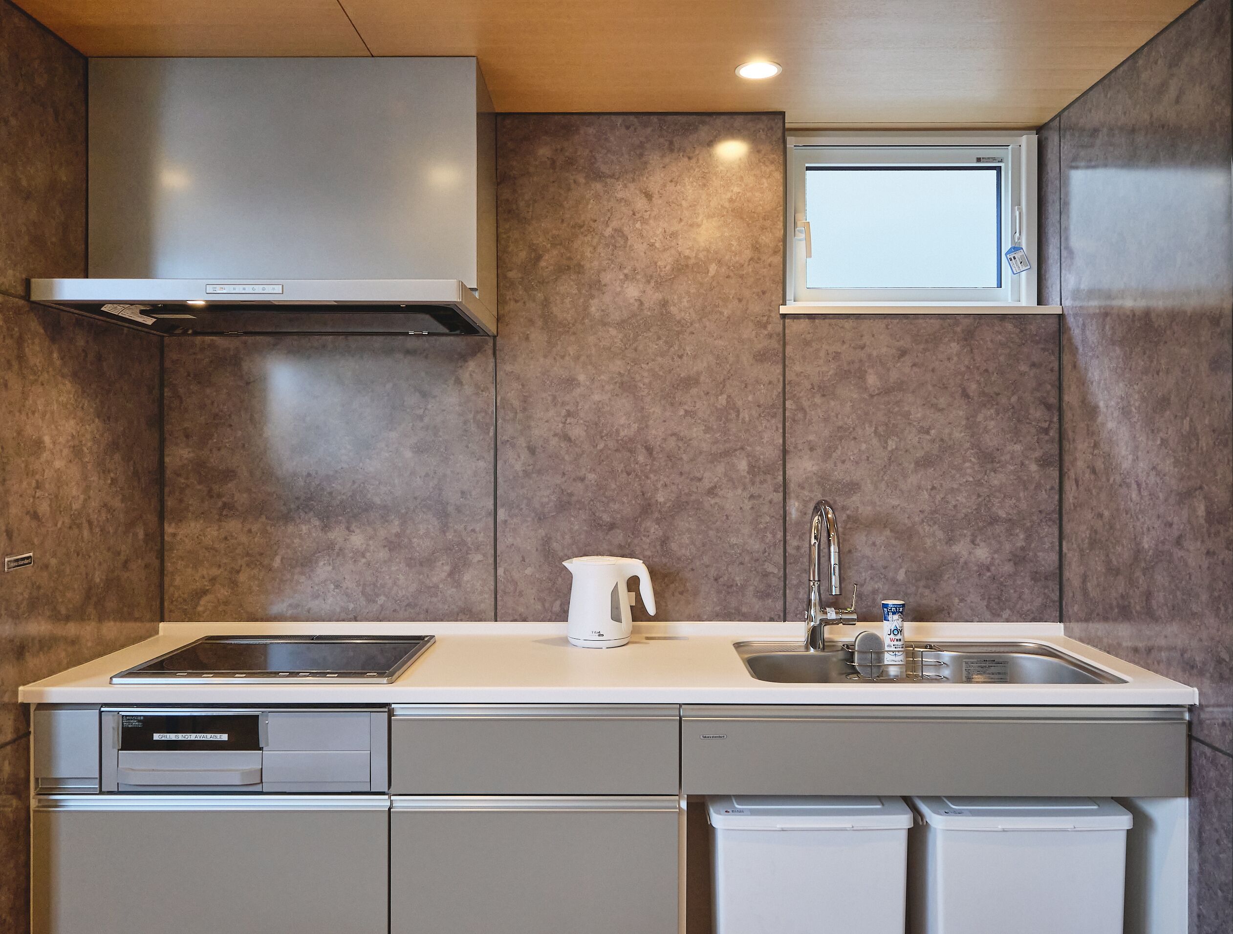 A modern kitchen with a built-in dishwasher, a stainless steel sink, and a window above the countertop.