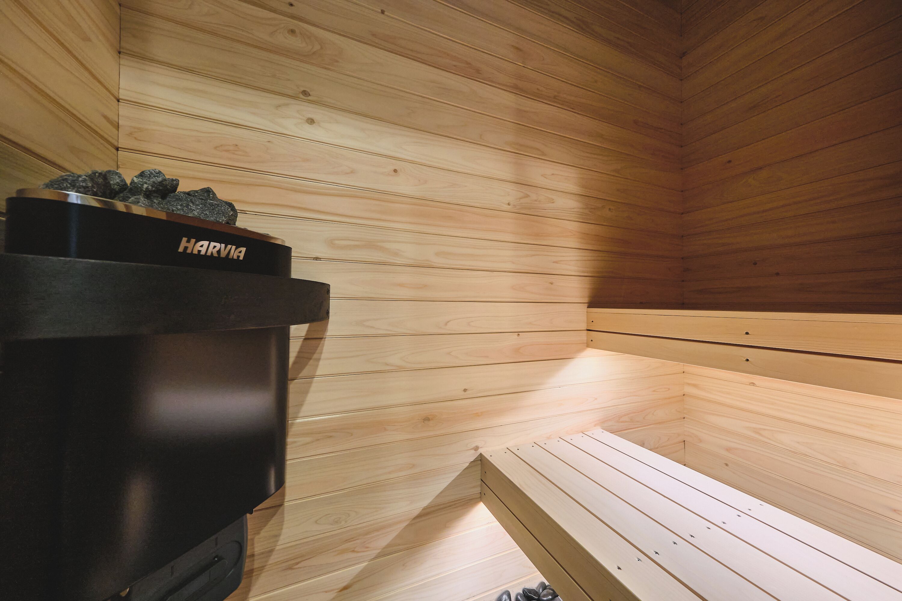 A sauna with wooden walls and benches, a Harvia sauna heater, and a small shelf with rocks.