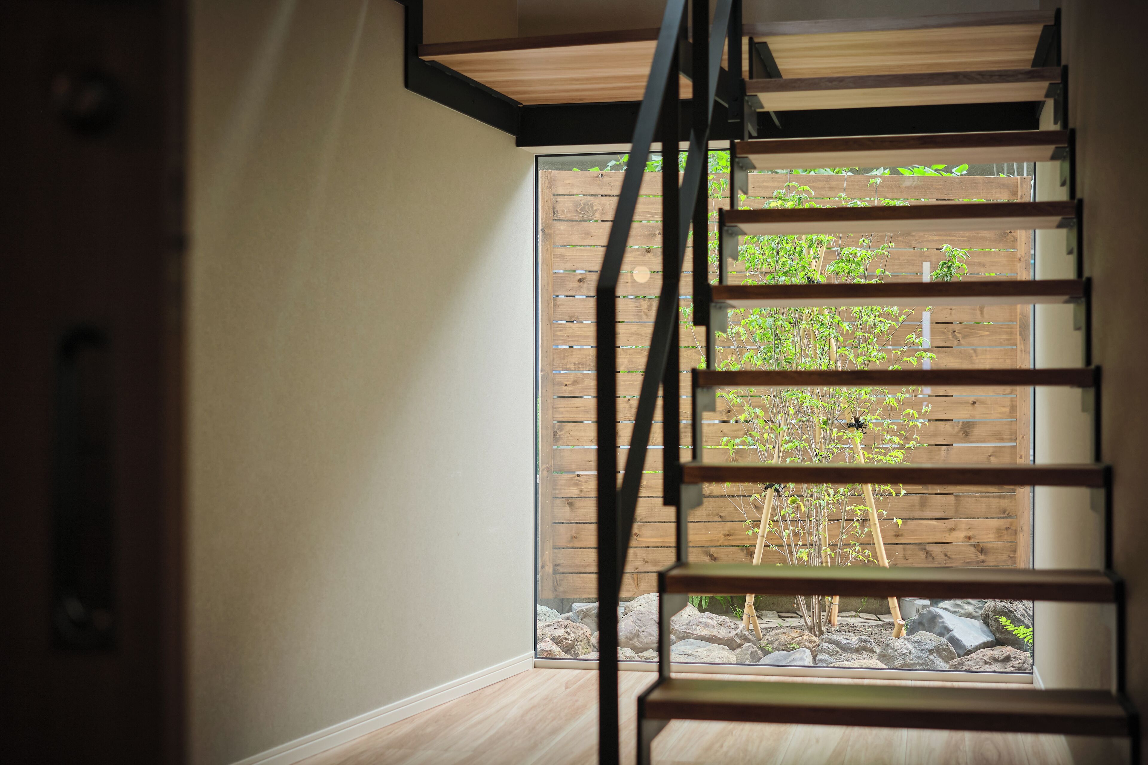 Un intérieur moderne avec un escalier en bois menant à une porte vitrée qui donne sur un jardin.