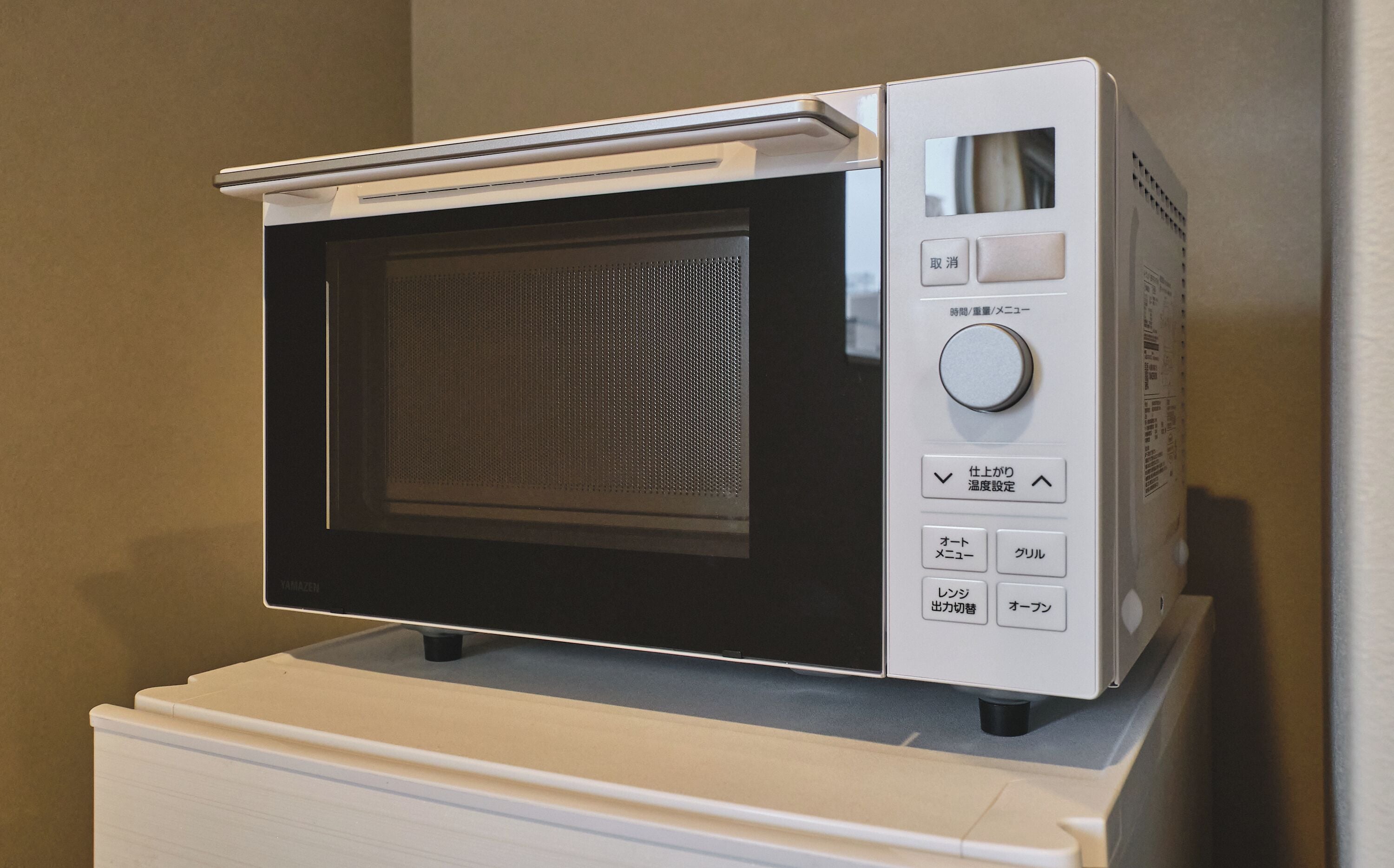 Un horno microondas blanco sobre un pedestal blanco, con pantalla digital y botones de control.