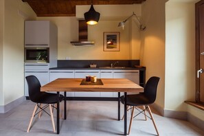 Een moderne keuken met een houten tafel, twee zwarte stoelen, een hanglamp en een magnetron boven het aanrecht.