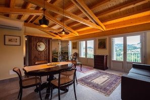 Un espace repas doté d’un plafond en bois, d’une table ronde, de chaises en osier et offrant une vue à travers de grandes fenêtres.