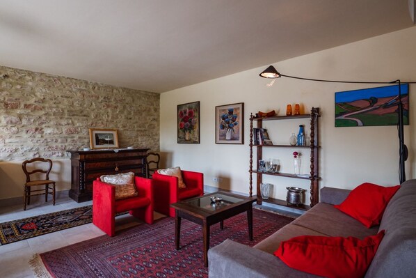 Un salon avec un mur en pierre, des canapés rouges et gris, une table basse en bois et une bibliothèque contenant divers objets.