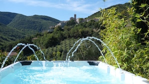 Ein Whirlpool mit Wasserstrahlen, umgeben von üppiger Vegetation und einer Bergkulisse.