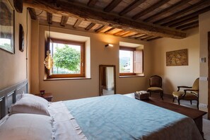 Une chambre avec un grand lit, deux fenêtres, un miroir, une chaise et un plafond en bois.