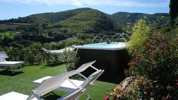 Ein Whirlpool umgeben von weißen Liegestühlen und einem Garten mit Blumen, mit sanften Hügeln im Hintergrund.