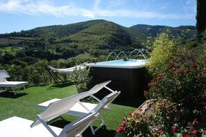 A hot tub surrounded by white lounge chairs and a garden with flowers, set against a backdrop of hills. - Villa le Moie by MMega (Arcevia)
