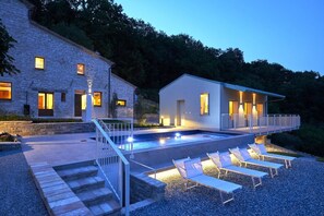 Een modern huis met een zwembad, terras en een stenen gebouw.