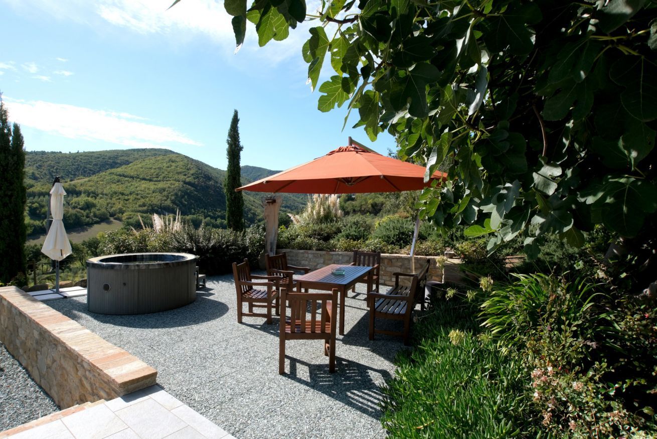 Une terrasse extérieure avec un jacuzzi, des meubles en bois et un grand parasol.