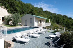 A poolside area with lounge chairs, a small building with a green roof, and a stone wall. - Villa le Moie by MMega (Arcevia)