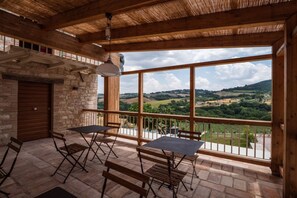 Un balcon en bois avec un mur en pierre, une porte en bois et une table avec des chaises.