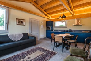A cozy living room with a sofa, a dining table with chairs, a kitchen area with cabinets, and a large window. - Villa le Moie by MMega (Arcevia)