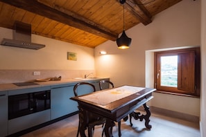 A kitchen with a wooden ceiling, a dining table with chairs, a window with a view, and a built-in oven. - Villa le Moie by MMega (Arcevia)