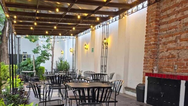 Een terras buiten met tafels en stoelen, lichtjes en bakstenen muren.