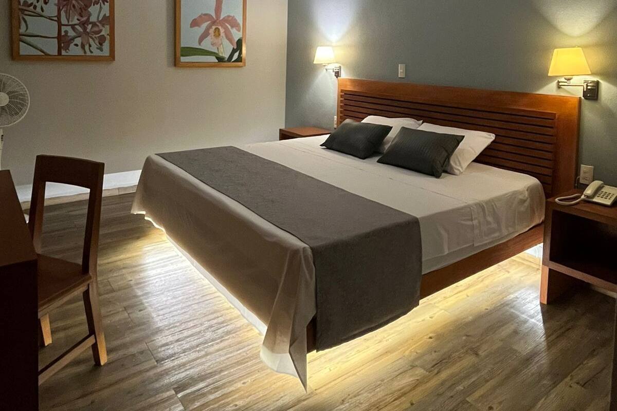 Een keurig opgemaakte slaapkamer met een bed, nachtlampjes, een stoel en een bureau.