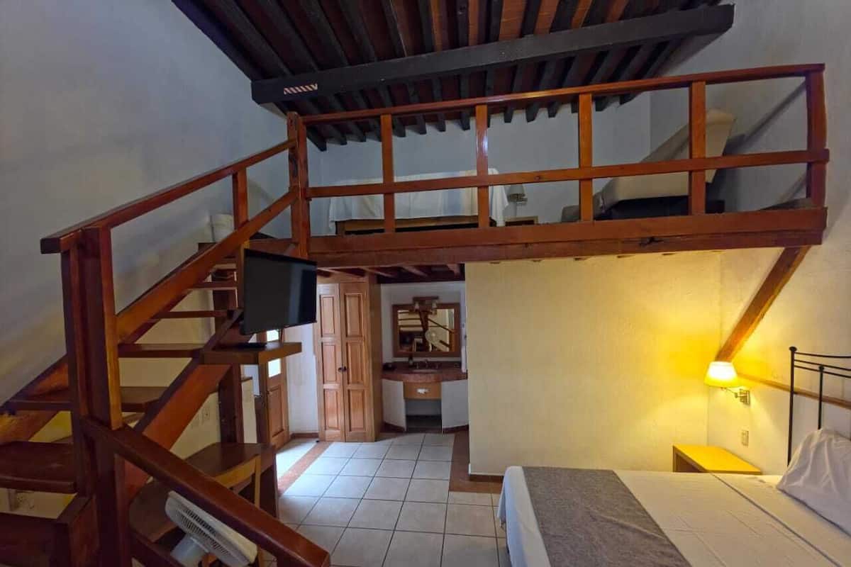 Een kamer met een stapelbed, een houten trap, een klein bureau en een spiegel.