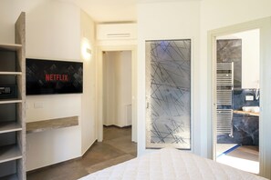 A modern hotel room with a bed, a TV mounted on the wall, a wardrobe, and a bathroom with a towel rack.