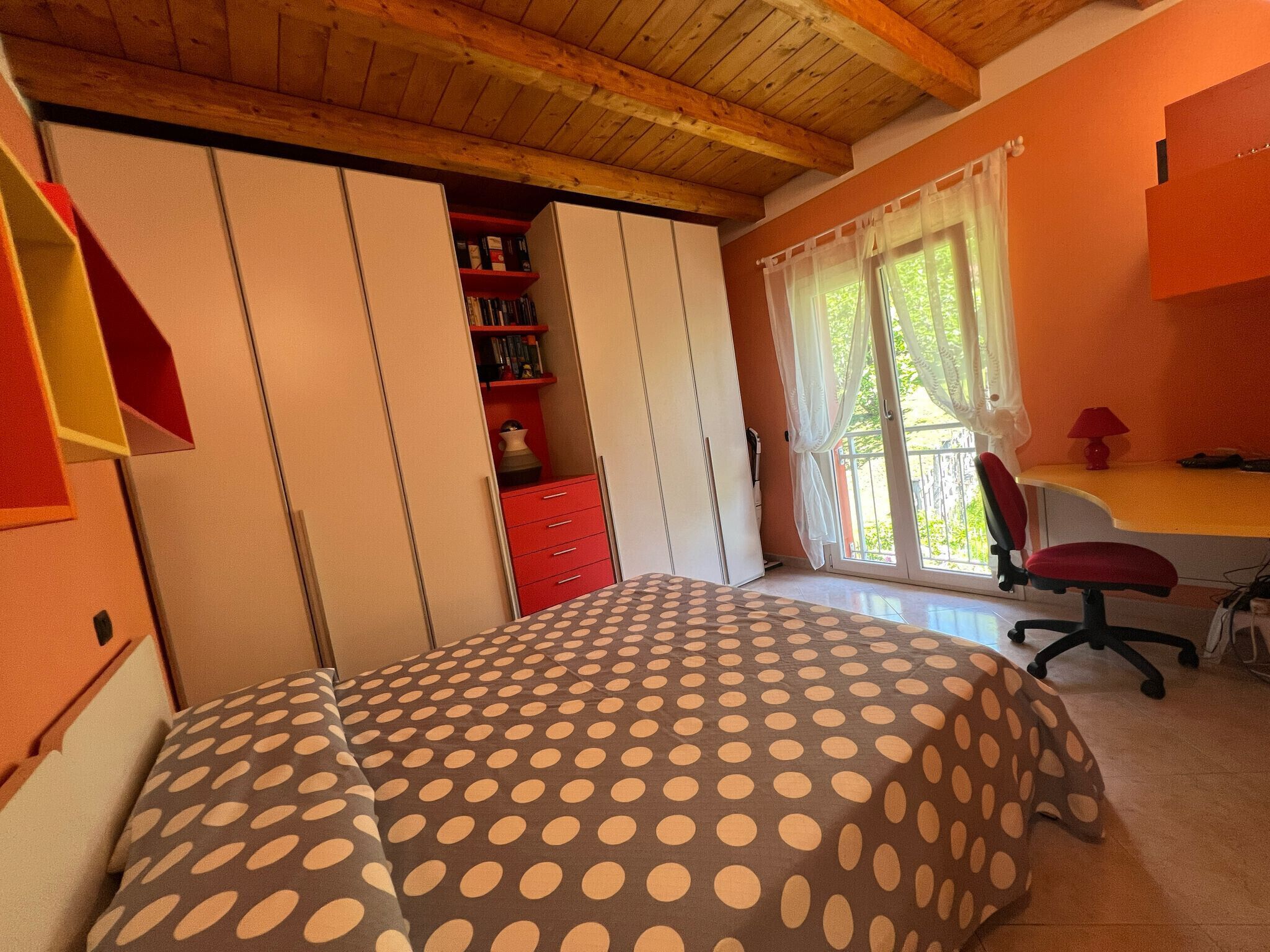 A bedroom with a bed, a desk, a chair, a wardrobe, and a window with curtains.