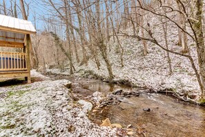 A wooden bench by a snow-covered stream in a forested area.