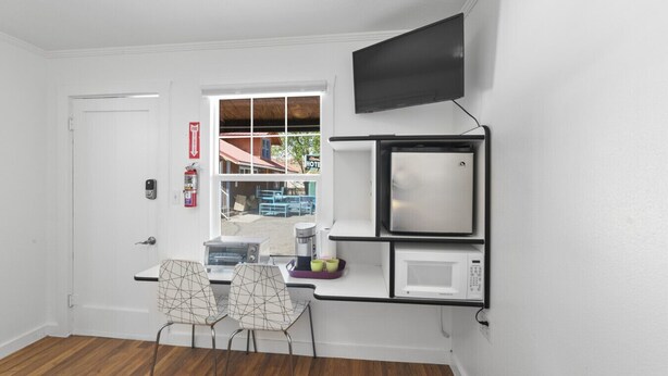 A compact hotel room with a kitchenette, a flat-screen TV mounted on the wall, a window with a view of the outside, and a door with a fire alarm. - Atomic #3 I Downtown I Historic I Trailer Parking (Moab)