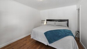 A bedroom with a bed, white walls, a wooden floor, a ceiling light, and a bedside table with a lamp. - Atomic #3 I Downtown I Historic I Trailer Parking (Moab)