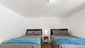 Een kamer met twee bedden, elk met hoofdeinde, een nachtkastje met lamp en een houten vloer.