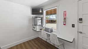 A compact kitchen with a microwave, toaster, and a small dining table with chairs. A fire extinguisher is mounted on the wall, and a door with a lock is visible. - Atomic #6 I Downtown I Historic I Trailer Parking (Moab)